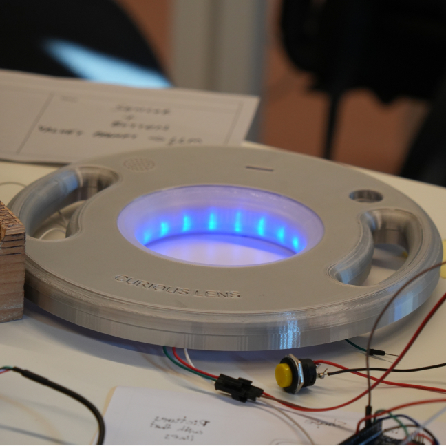 A grey Curio lying flat with its LED ring glowing blue